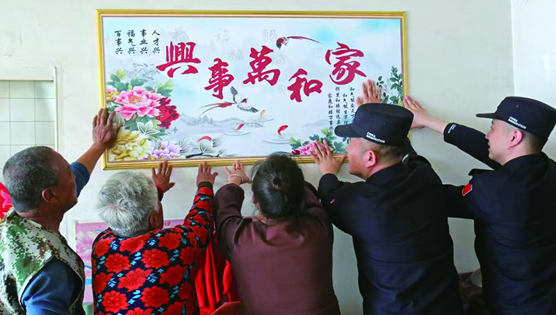 二题图，民警和这一家人一起把“家和万事兴”挂画贴上墙