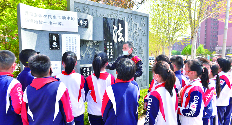 头题图，普法志愿者在宪法墙前给学生们普及法律知识。