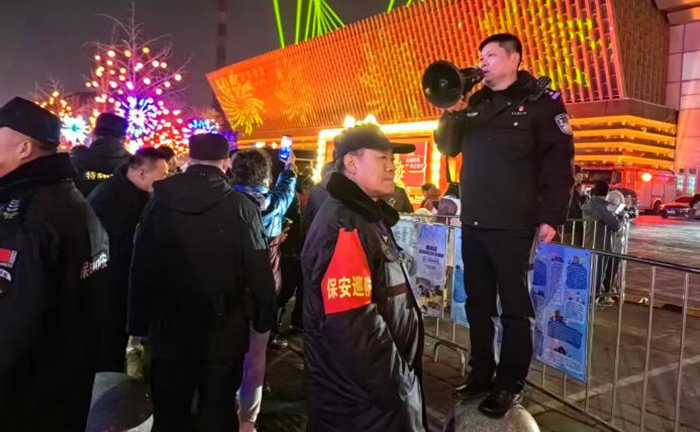 夜间大型群众活动现场，李斌站在石墩上手持喇叭疏导人流，联合保安维护现场秩序